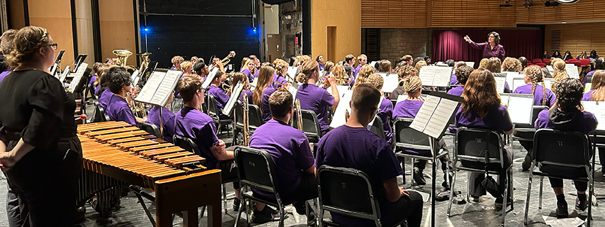 A conductor leading a group of band members on stage